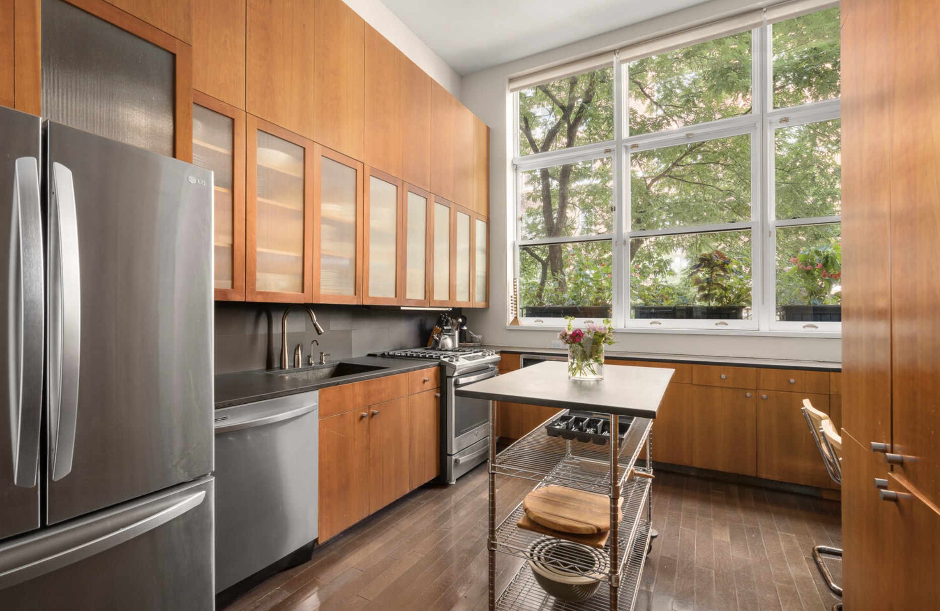 Kitchen with wood cabinets, stainless steel appliances, a rolling island and tall windows overlooking trees