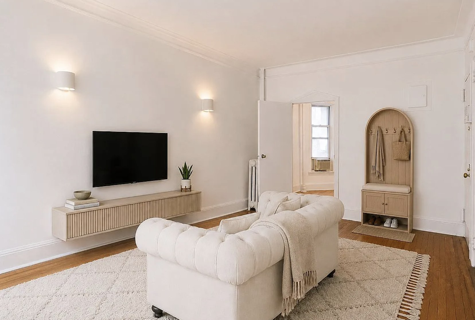 Bright Yorkville one-bedroom living room with a white tufted sofa, wall-mounted television and hardwood floors