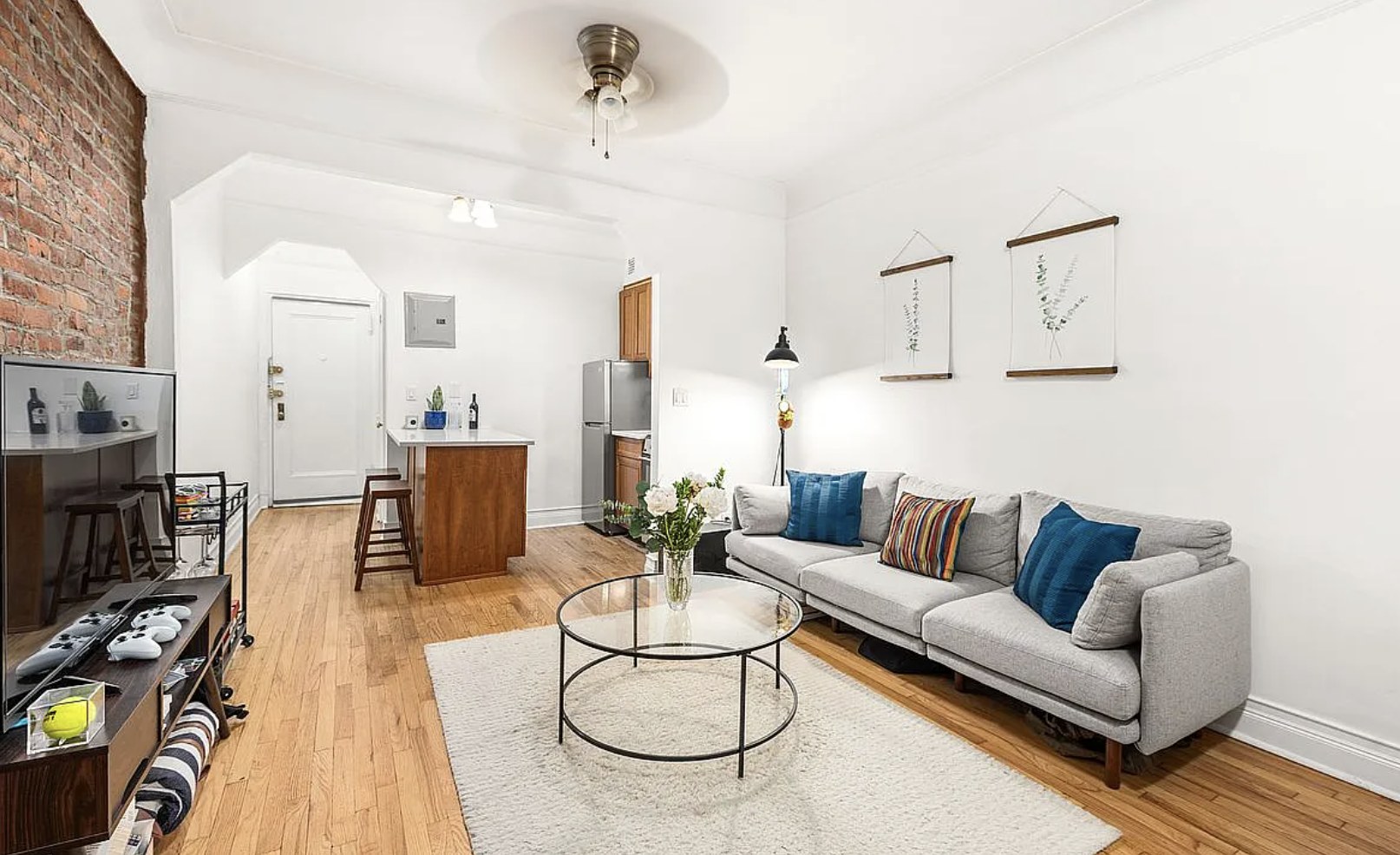 Bright Yorkville studio with an exposed brick wall, hardwood floors, a gray sofa and a kitchen island with stools